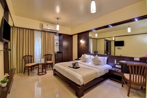 A hotel room with a large bed, a desk, two chairs, a TV, and a mirror. - Hotel Lotus Ivy Studios,Near Pune Airport (Pune)