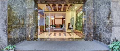 A hotel entrance with marble walls, a glass door, and a reception area visible through the glass.
