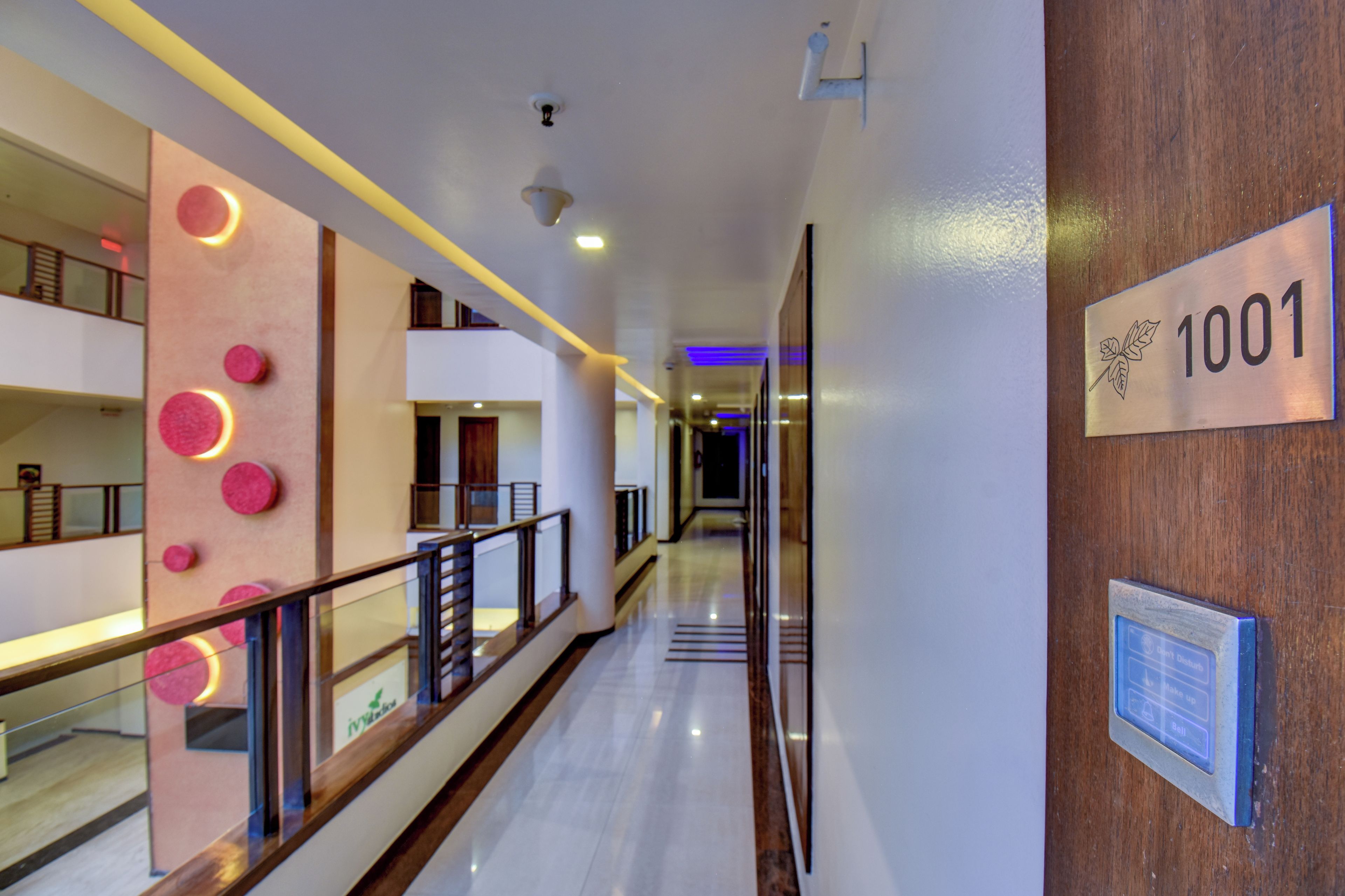 A hotel corridor with a modern design, including a railing, a sign with the number 1001, and a blue-lit hallway.