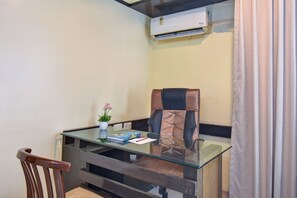 A small office space with a glass desk, a leather chair, a potted plant, and an air conditioning unit mounted on the wall. - Hotel Lotus Ivy Studios,Near Pune Airport (Pune)