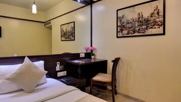 A hotel room with a bed, bedside table, chair, artwork, and a desk with a plant.