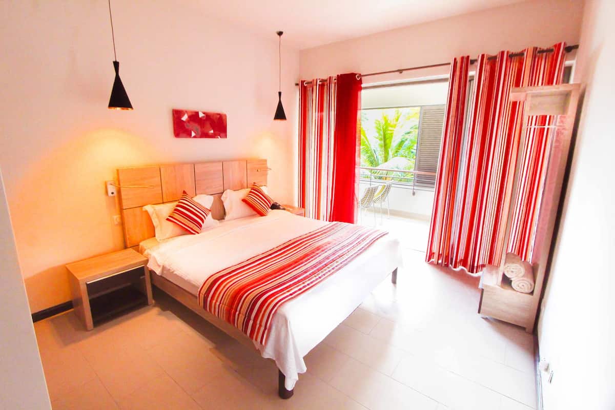 A bedroom with a bed, bedside table, and a view of the outdoors through a window with curtains.