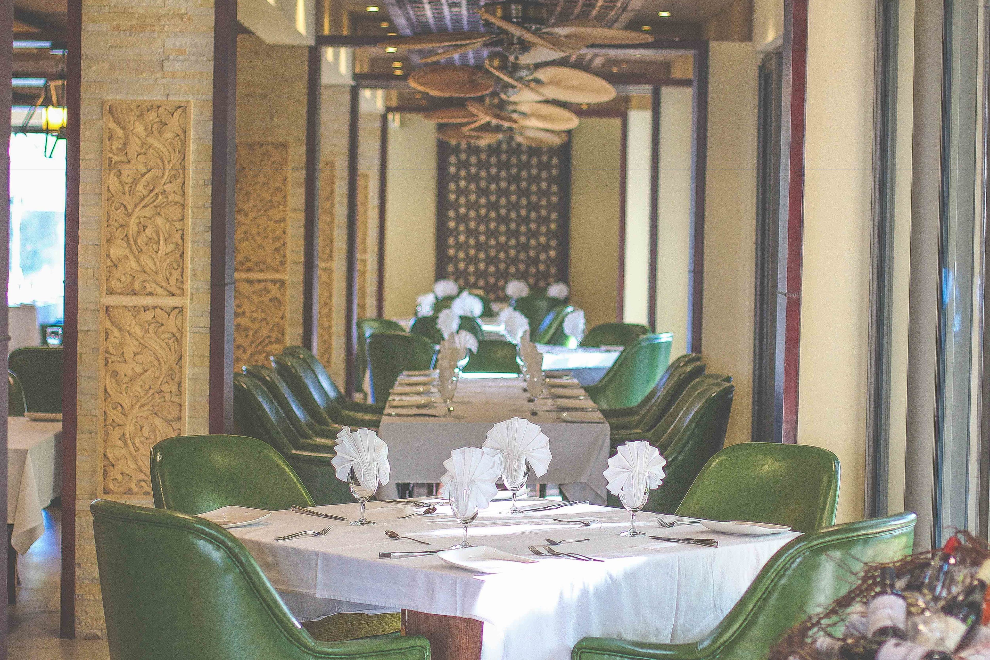 A restaurant with a long table set for a meal, green chairs, and a decorative wall.