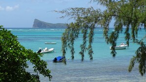 A coastal scene with clear turquoise waters, boats, and a prominent mountain in the background. - Nitzana Residences & Restaurant (Cap Malheureux)