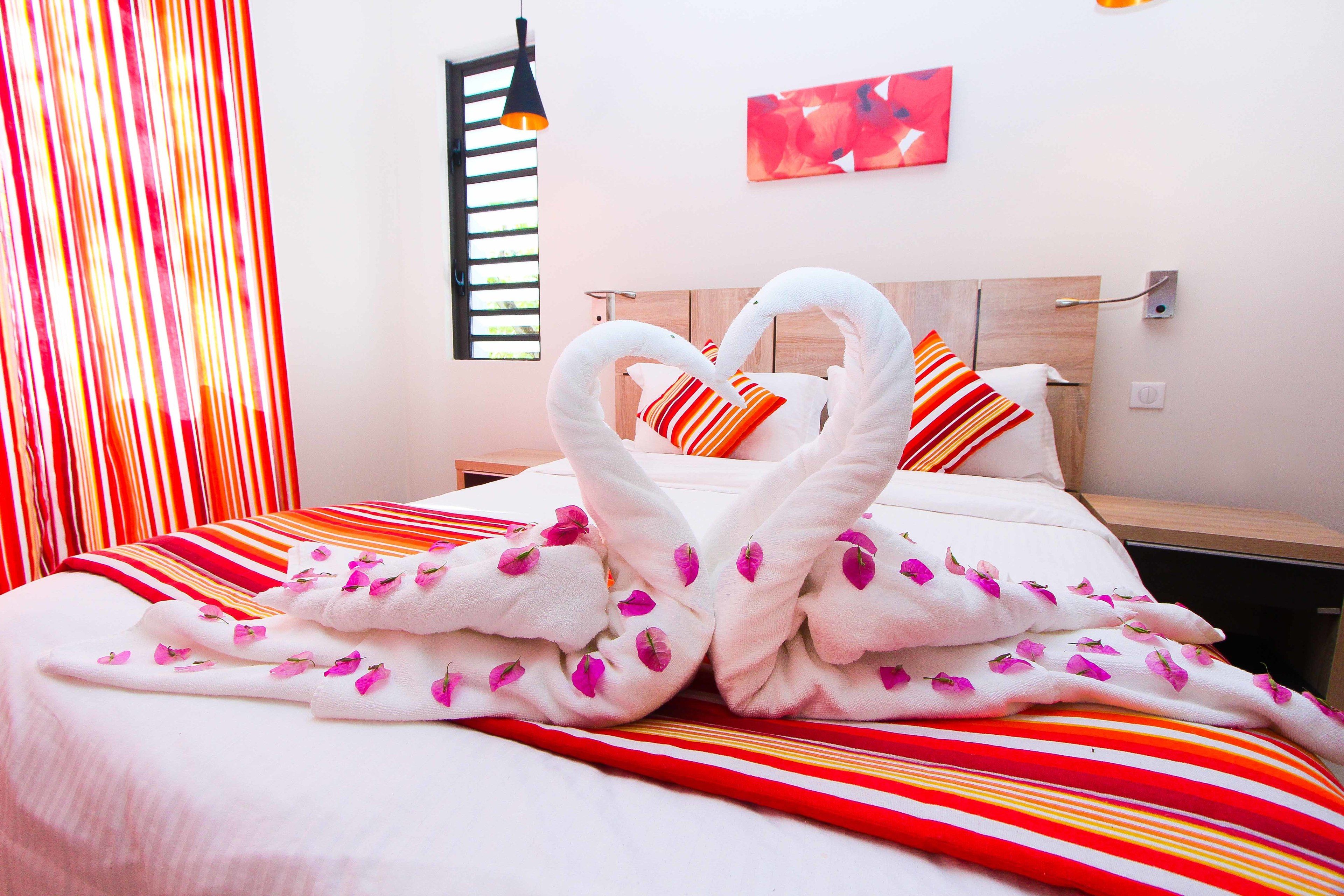 A hotel room with a bed featuring a heart-shaped towel arrangement and a striped blanket.