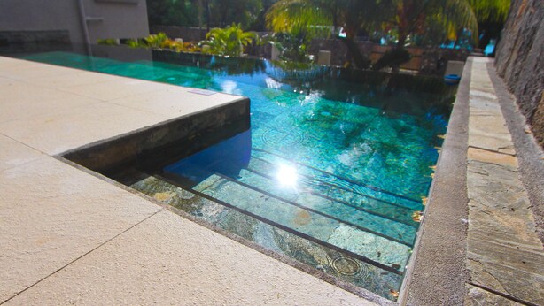 A clear swimming pool with a tiled deck and a stone wall. - Nitzana Residences & Restaurant (Cap Malheureux)