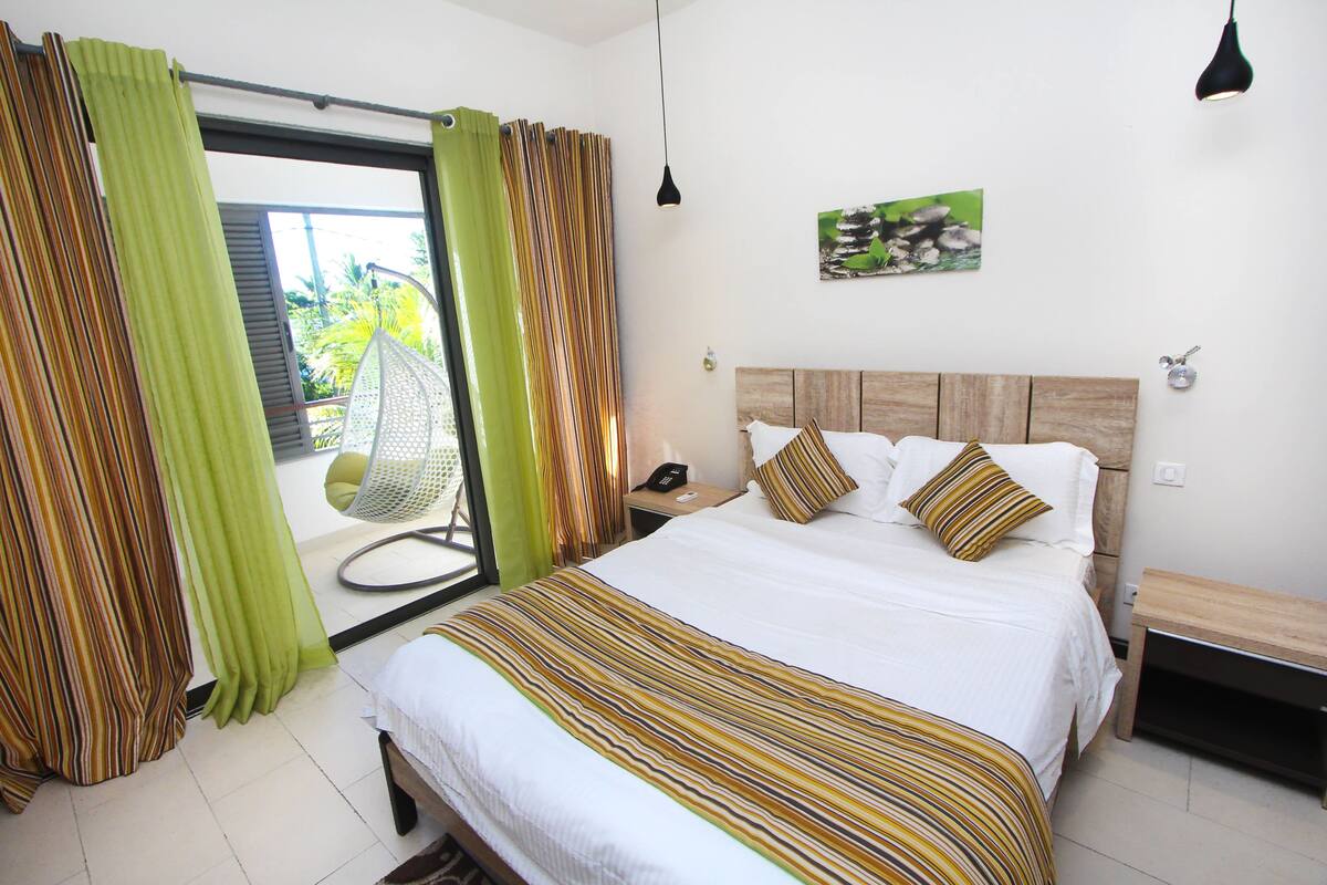 A hotel room with a large bed, a wooden headboard, a nightstand, and a view of the outdoors through a sliding door.