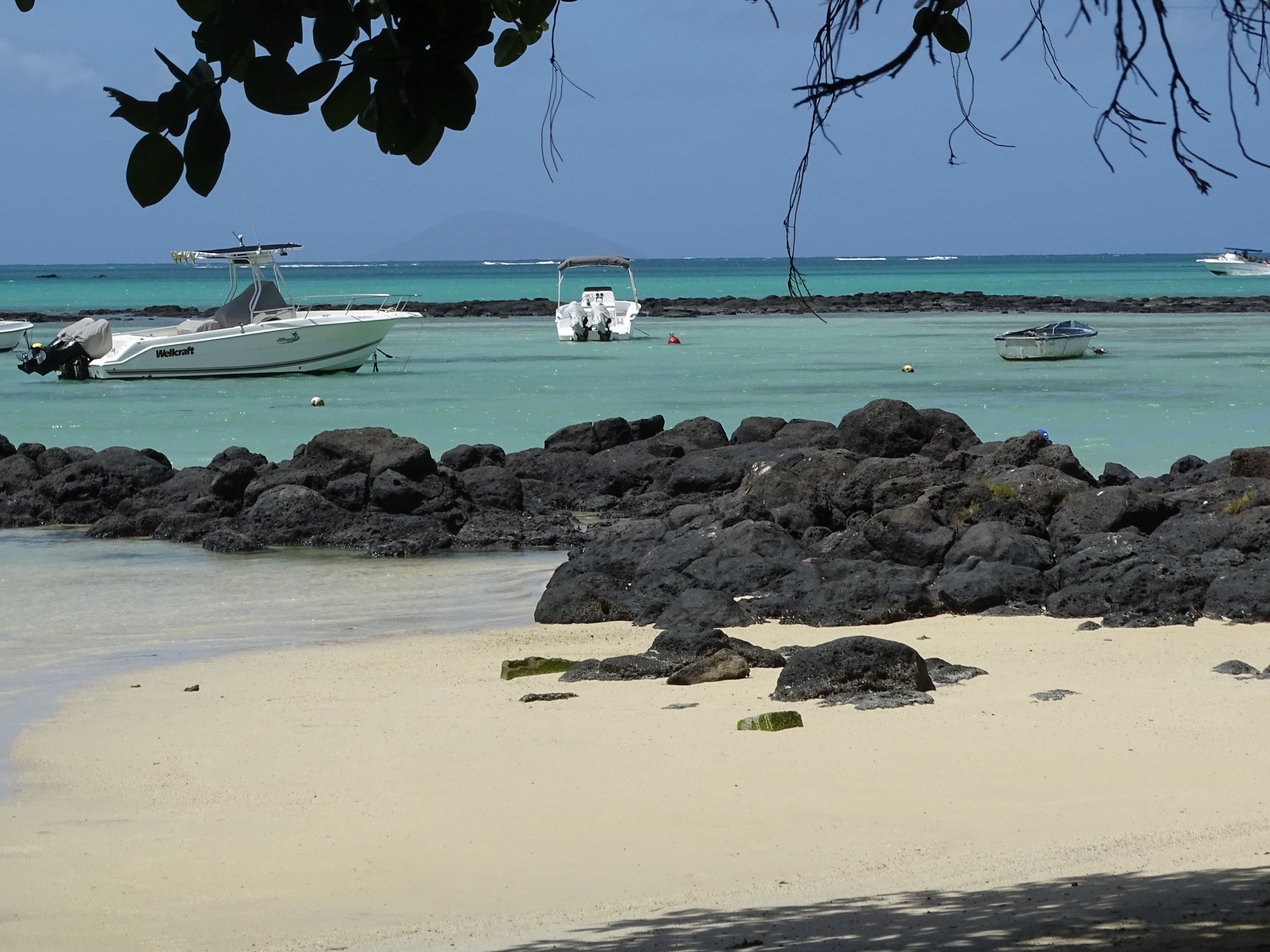 A beach with boats anchored near the shore, surrounded by dark volcanic rocks.