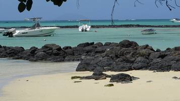 Una playa con barcos anclados cerca de la orilla, rodeada de oscuras rocas volcánicas.