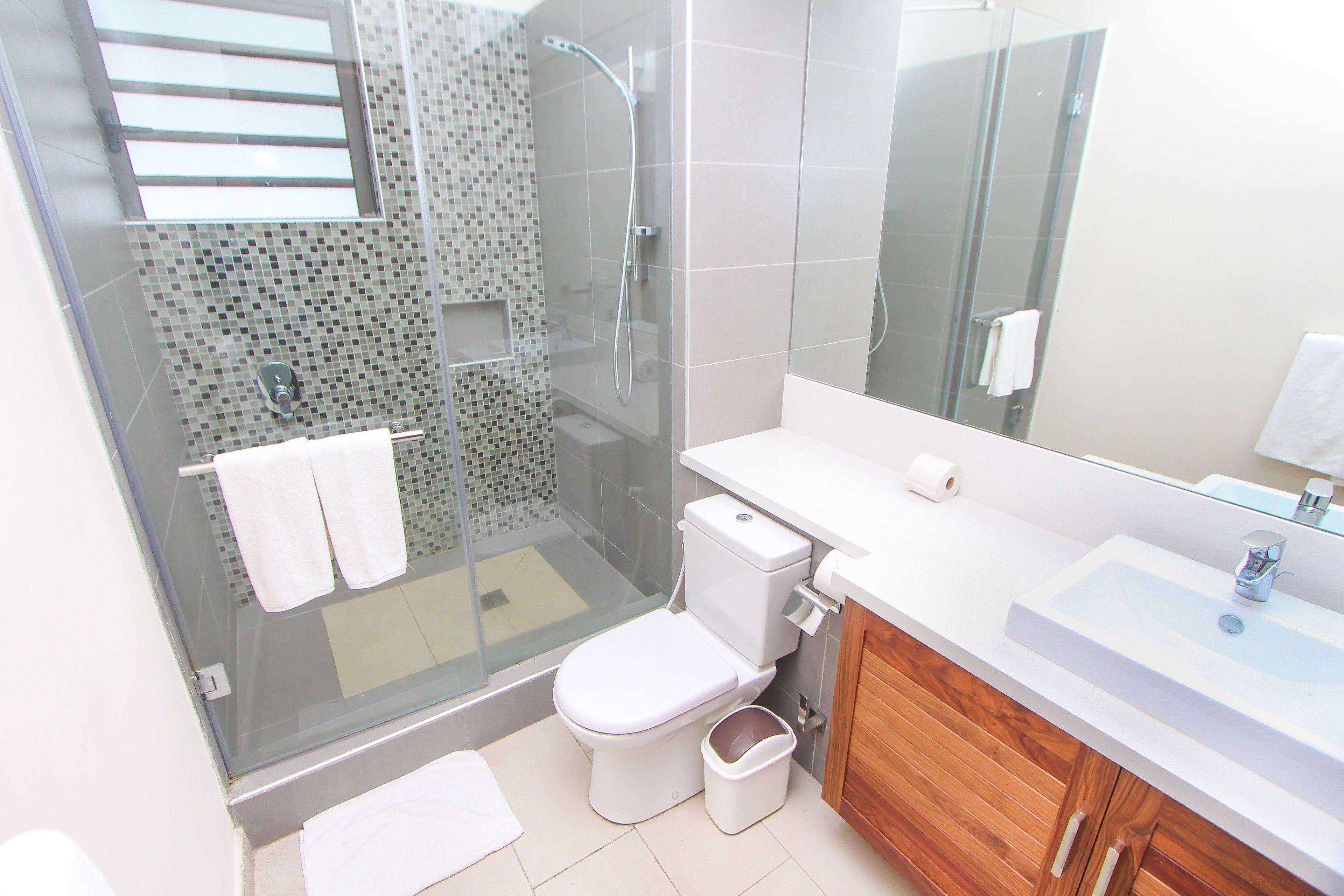 Un baño moderno con ducha envuelta en vidrio, inodoro blanco y tocador de madera con lavamanos.