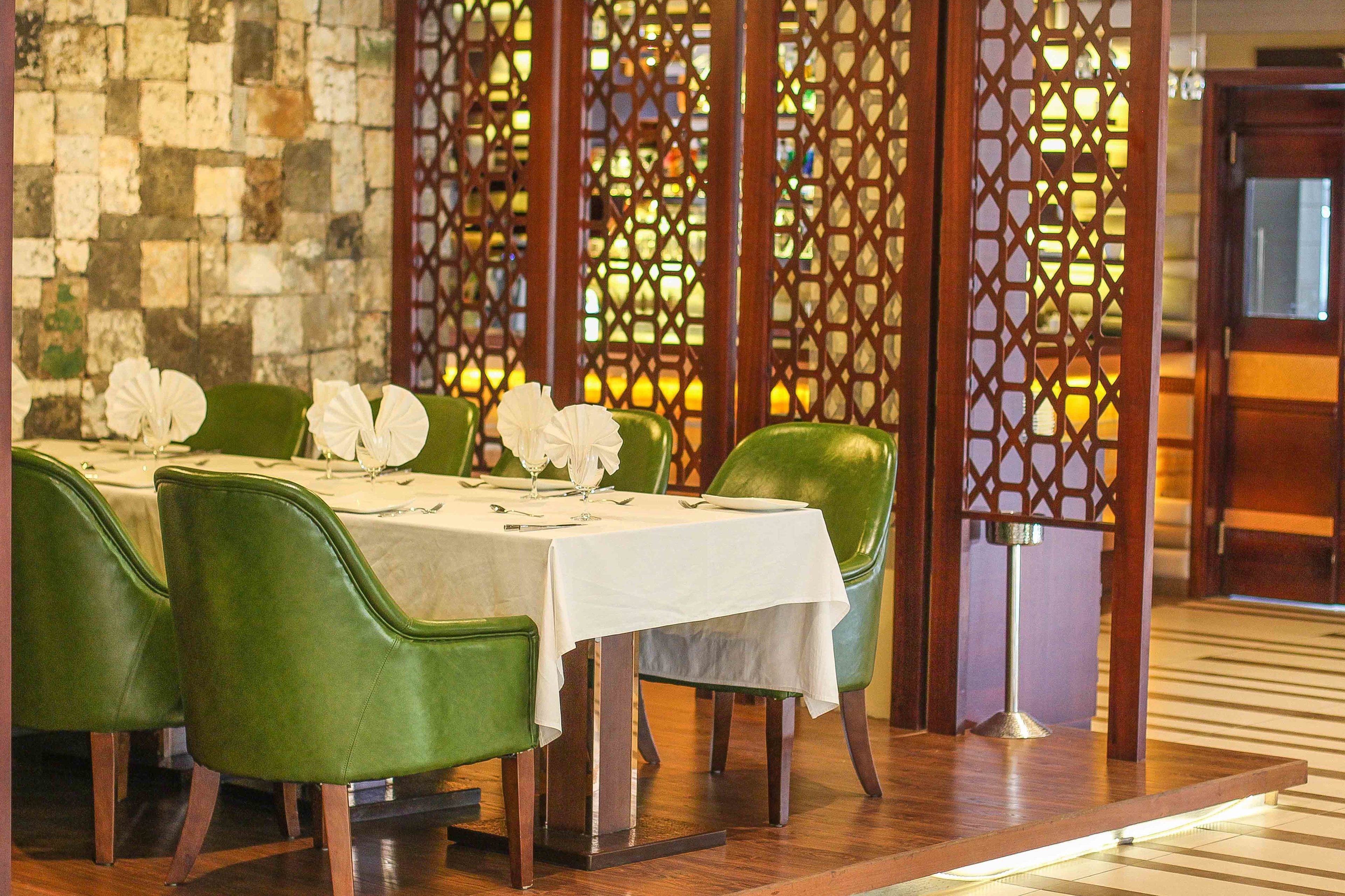 Comedor con sillas verdes y manteles blancos, paneles de madera y una pared de piedra.