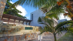 A stone wall with a green plaque, a palm tree, and a modern building with a flat roof. - Nitzana Residences & Restaurant (Cap Malheureux)