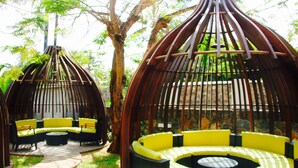 A garden area with outdoor seating under wooden structures, surrounded by trees. - Nitzana Residences & Restaurant (Cap Malheureux)