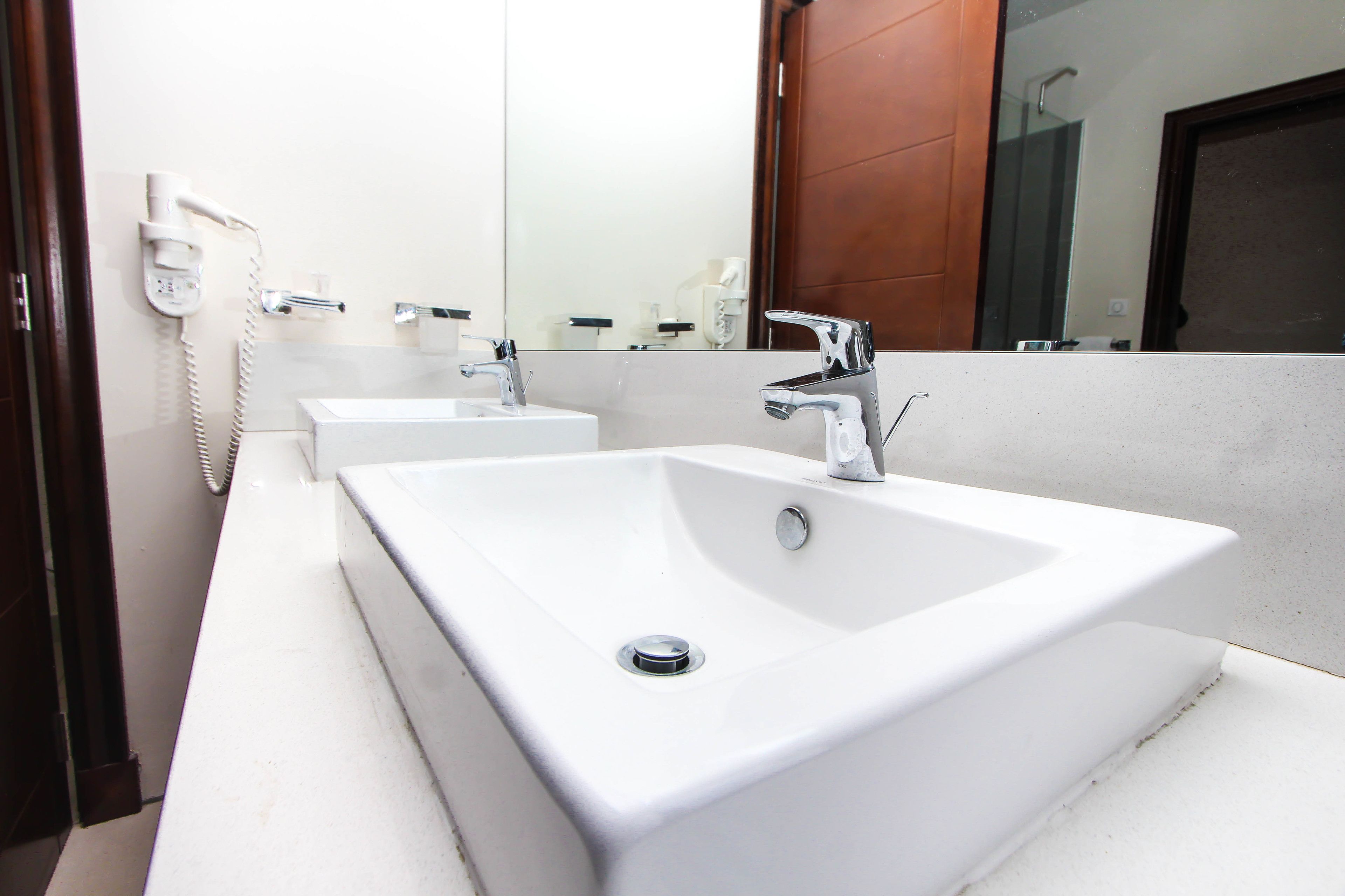 Une salle de bain moderne avec deux lavabos, un miroir et un sèche-cheveux fixé au mur.