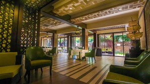 A spacious lobby with a patterned ceiling, green upholstered seating, and a view of the outdoors through large windows. - Nitzana Residences & Restaurant (Cap Malheureux)