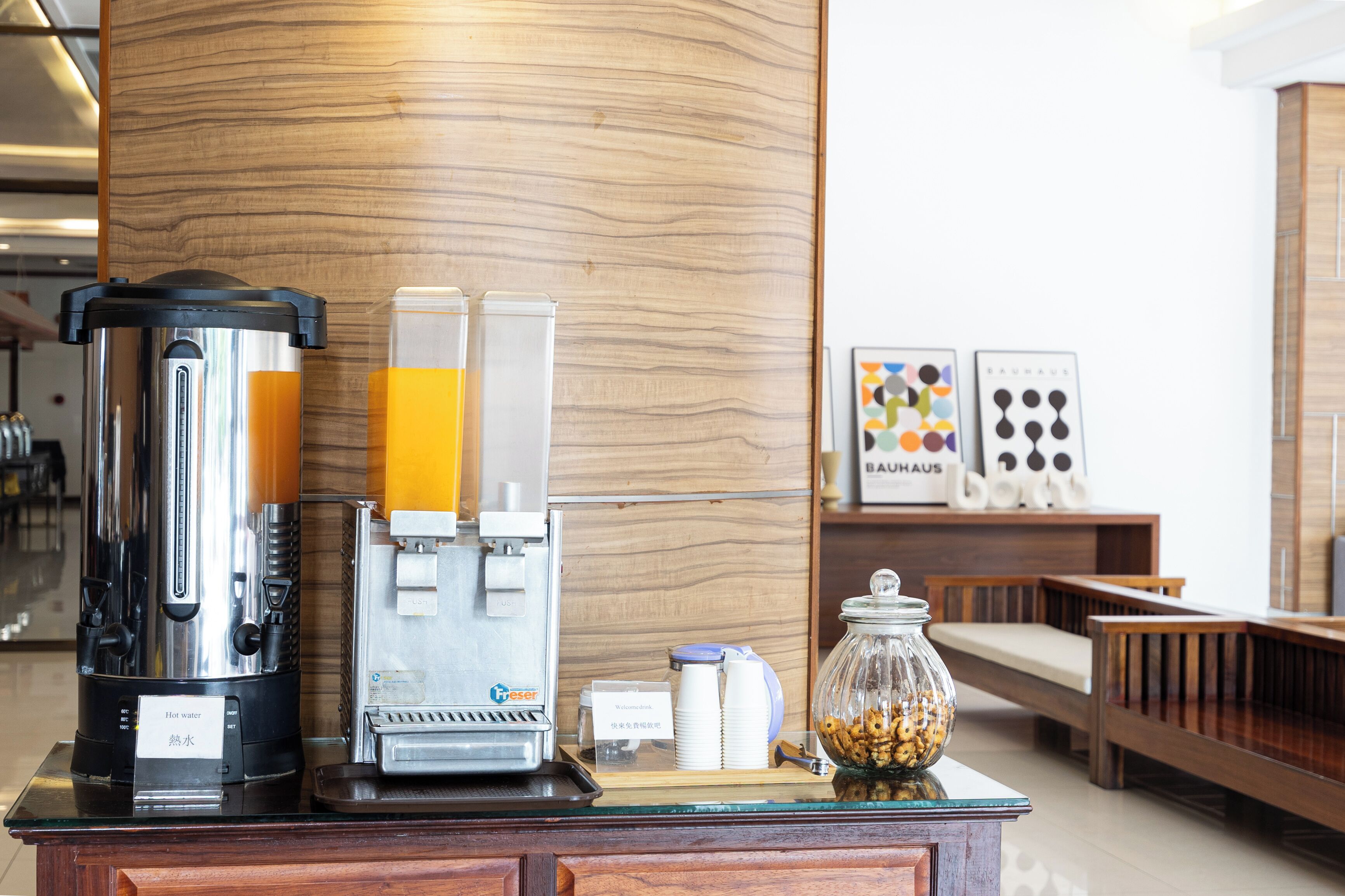 A coffee station with a hot water dispenser, a coffee machine, and a jar of nuts.