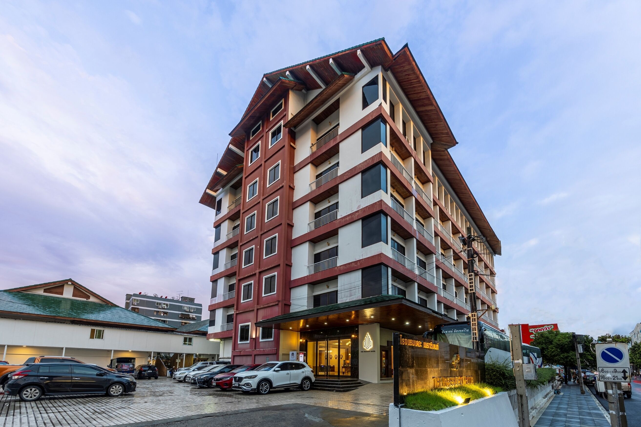 Un hôtel à plusieurs étages, doté d’un design moderne, avec une entrée imposante et un parking pouvant accueillir plusieurs voitures.