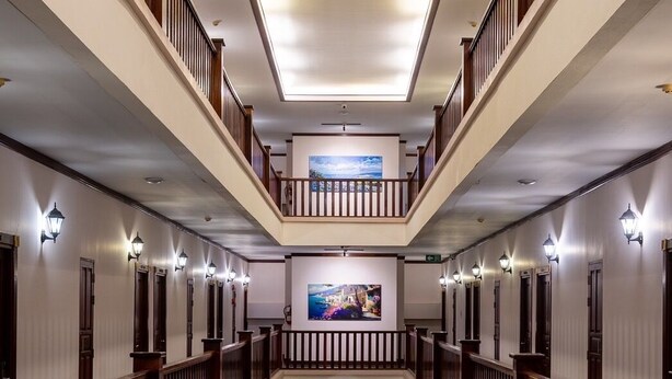 Hall d'ingresso di un hotel su più livelli, con una scalinata centrale, ringhiere in legno e opere d'arte alle pareti.