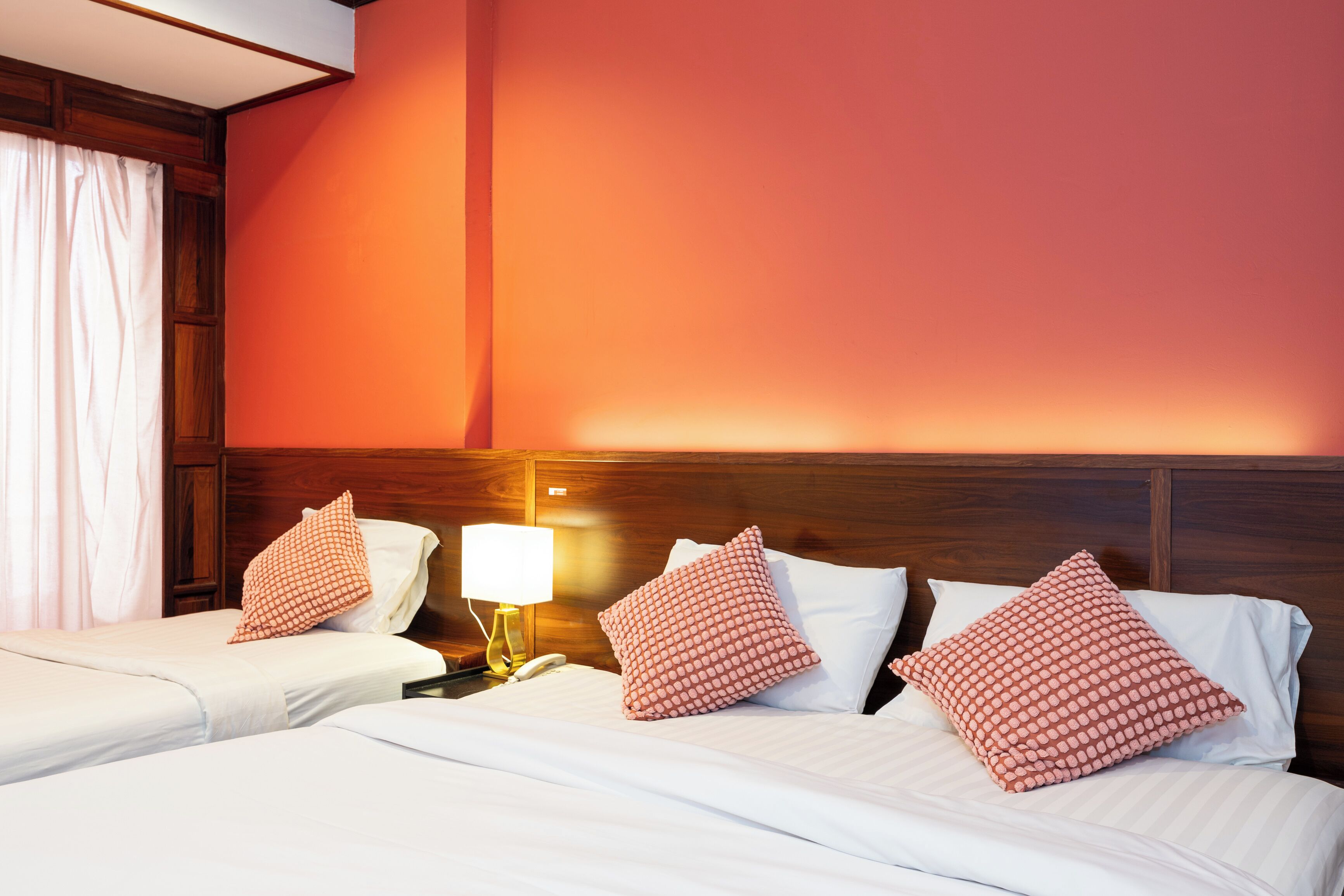 A hotel room with two beds, a nightstand with a lamp, and a wooden headboard.