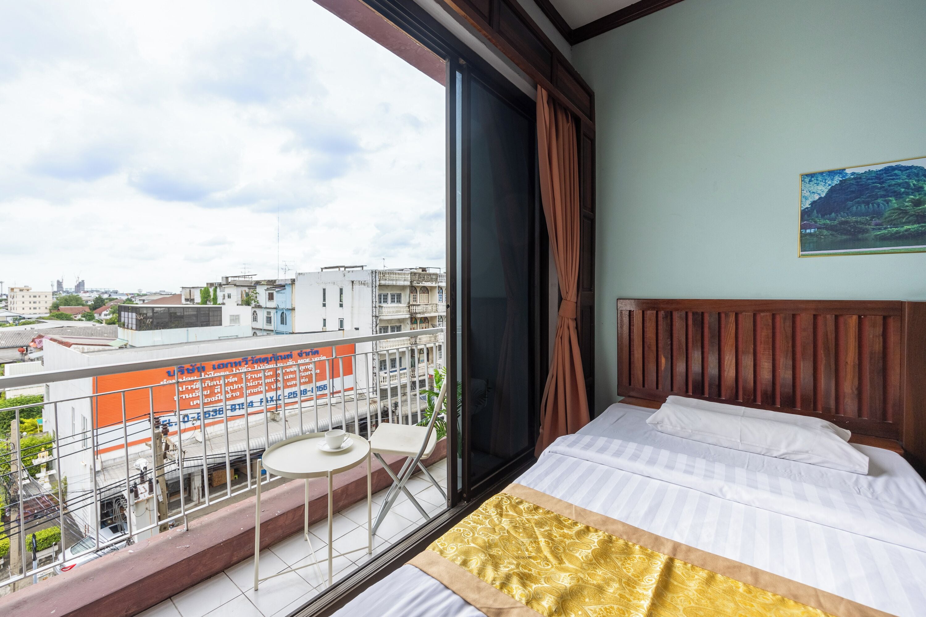 A hotel room with a large window, a balcony with a table and chairs, and a bed with a patterned bedspread.