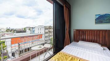 A hotel room with a large window, a balcony with a table and chairs, and a bed with a patterned bedspread.