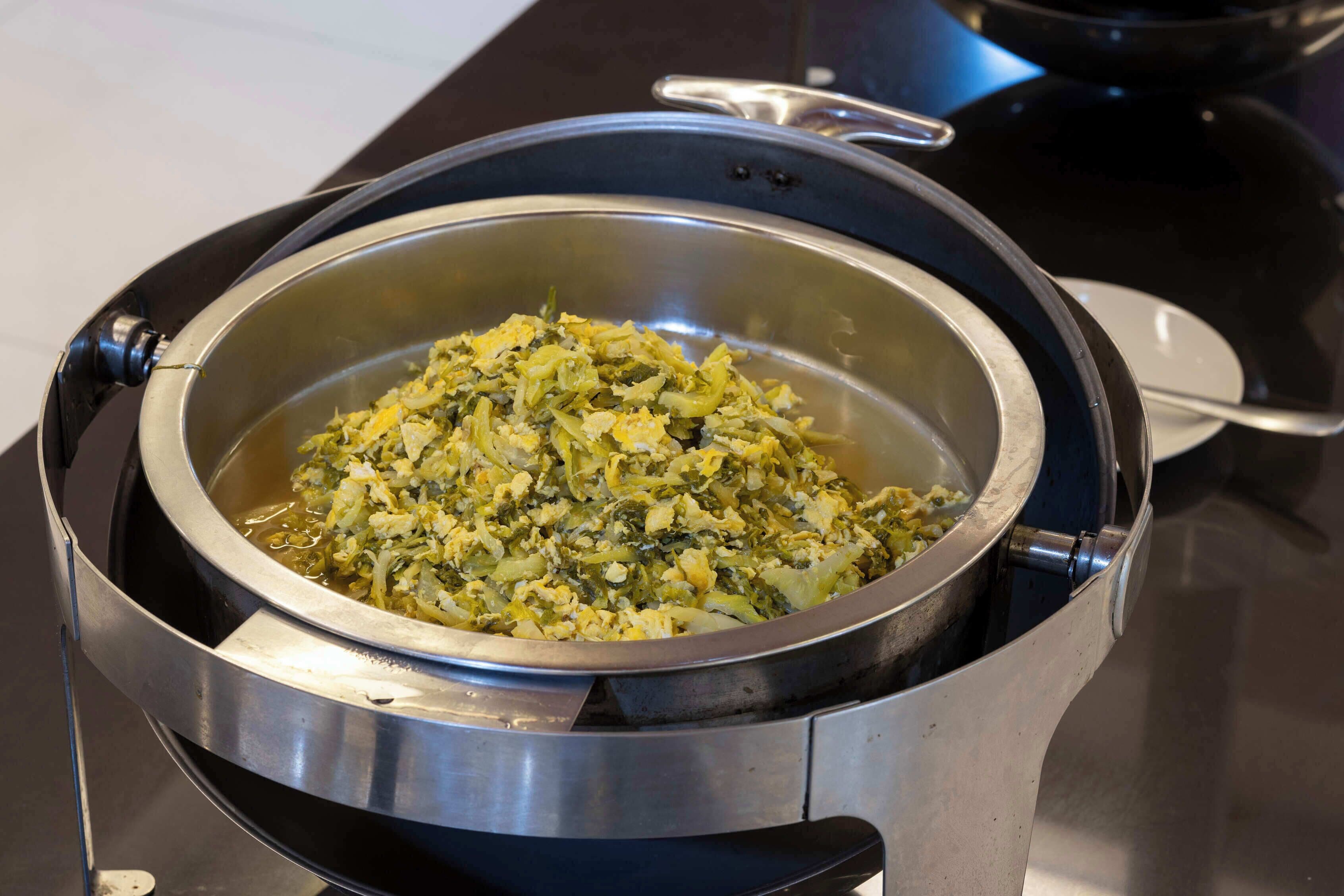 A stainless steel pot containing a dish with green vegetables and possibly eggs.