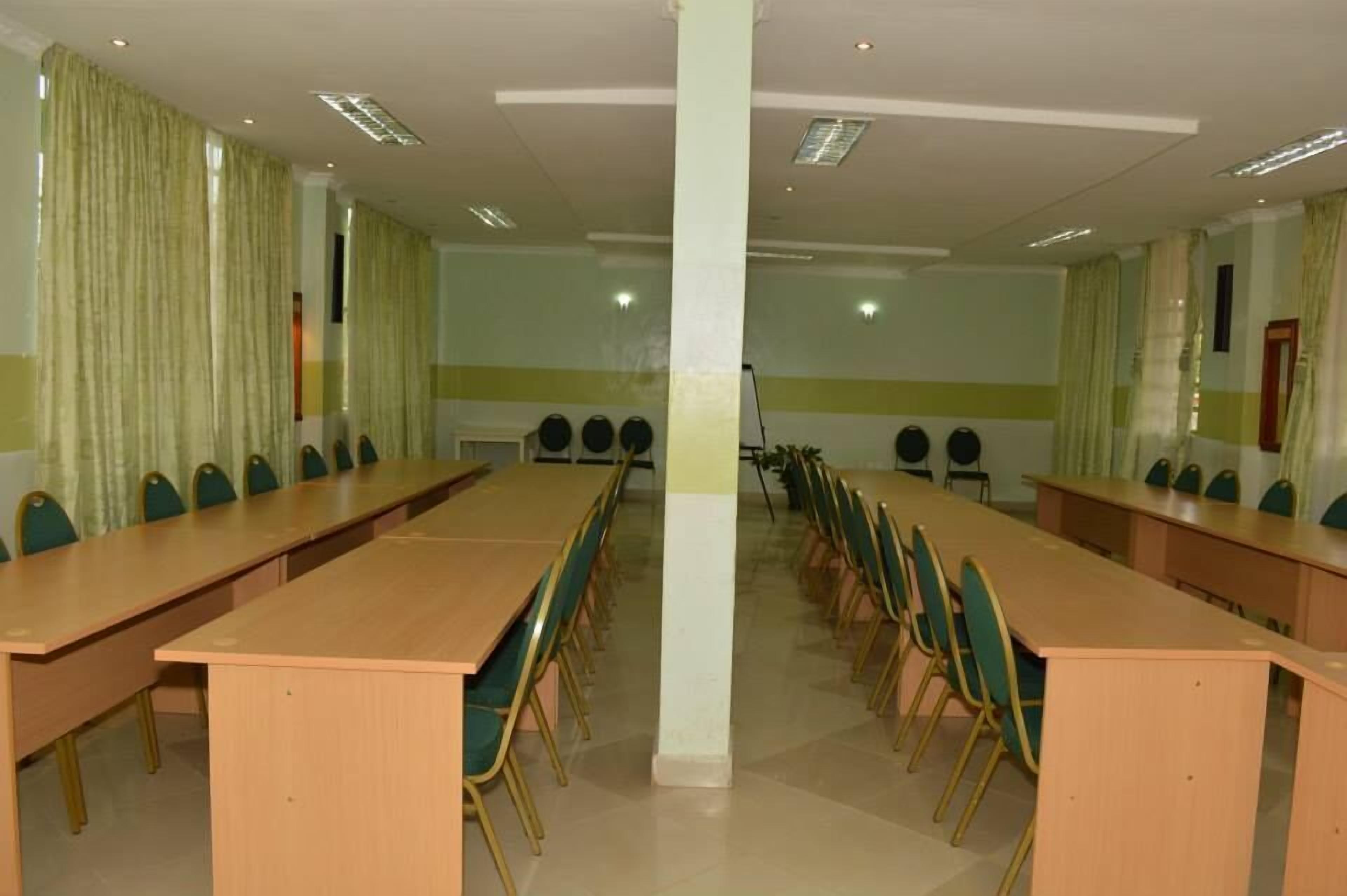 A conference room with long tables and chairs, a white pillar, and curtains.