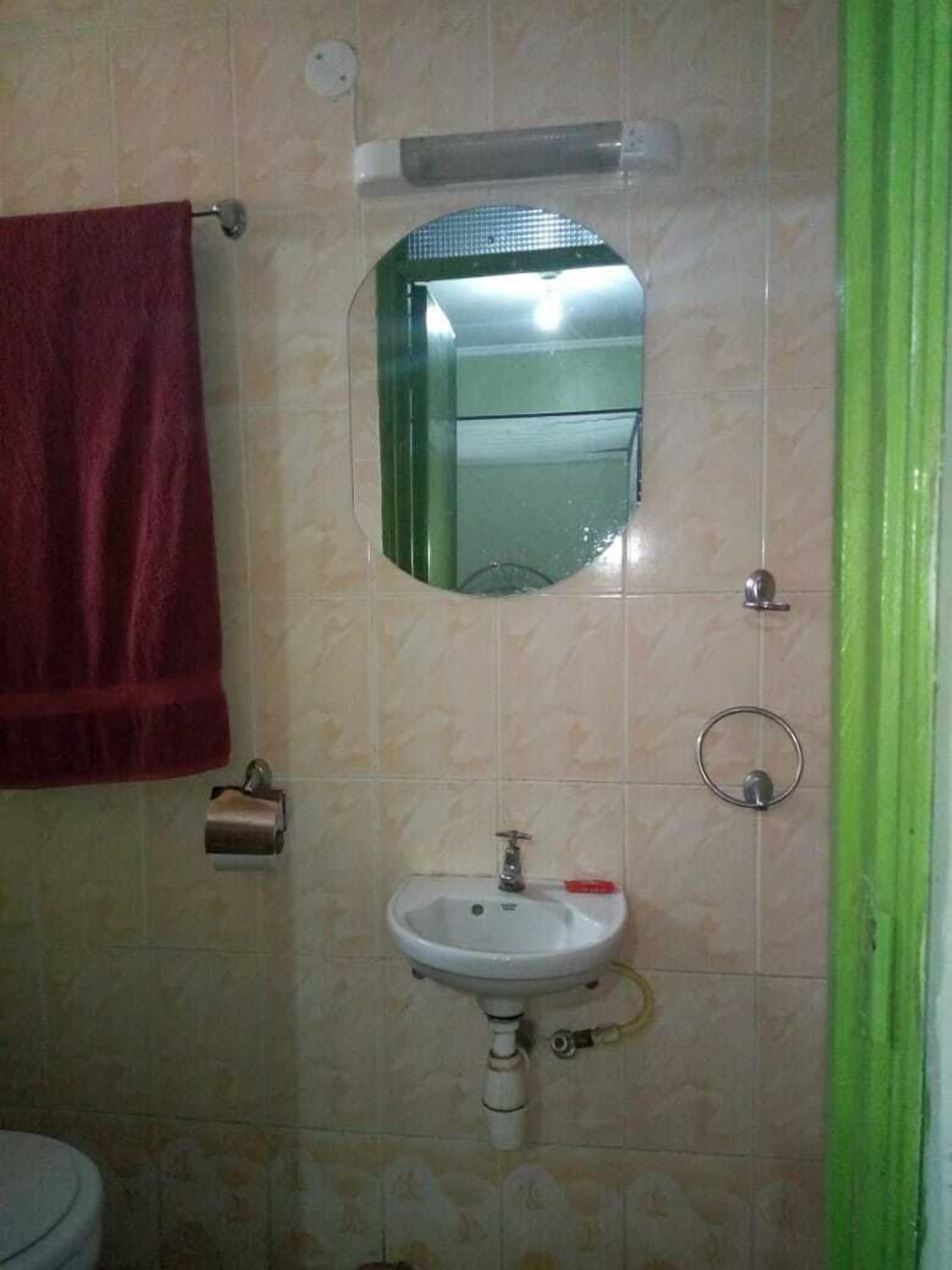 Un baño con lavamanos blanco, un espejo, una toalla roja y una cortina verde.