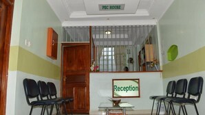 A reception area with a sign that reads "Reception," a wooden door, and several black chairs arranged around a glass table. - PEC Guest House (Ngong)