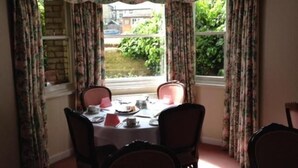 A dining area with a table set for four, surrounded by chairs, and a window with curtains. - Ashley Hotel (Cambridge)