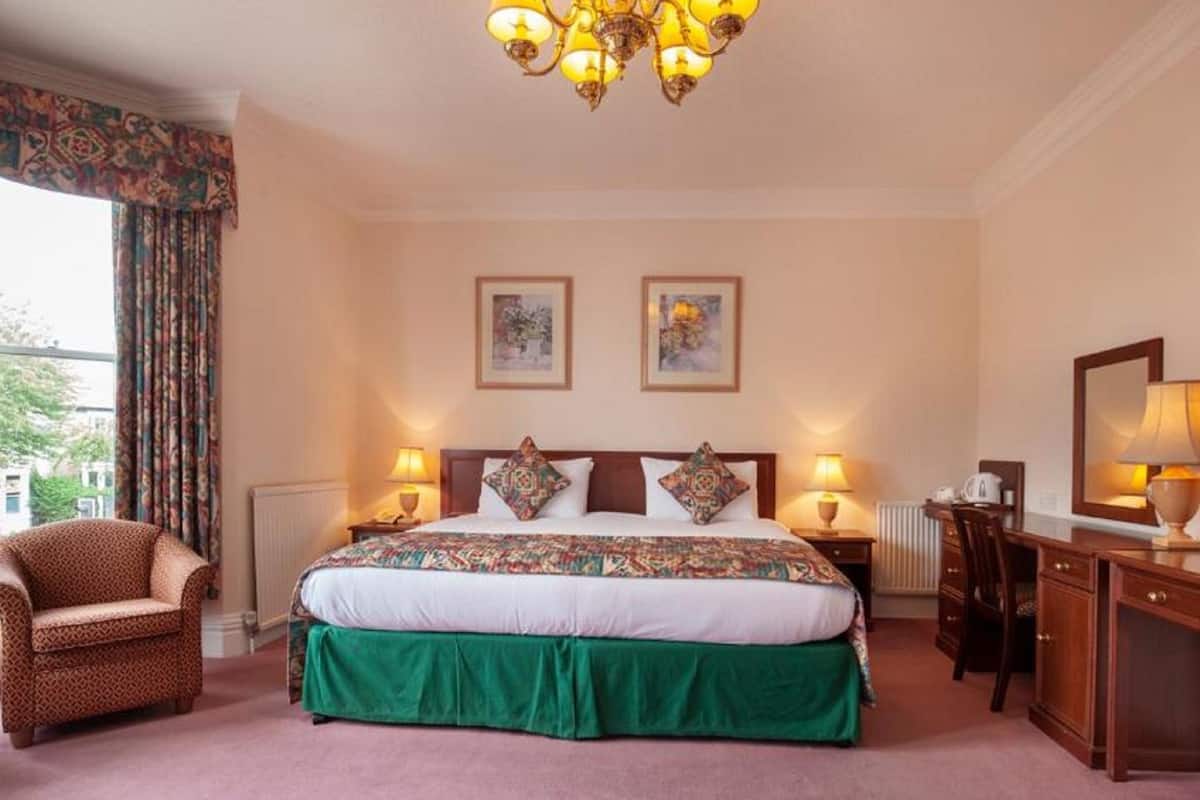 A hotel room with a large bed, two bedside lamps, a chair, a desk, and a mirror.