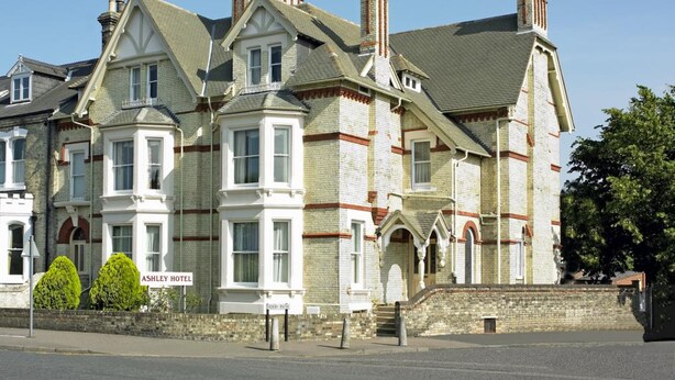 A large, historic building with multiple chimneys, a prominent bay window, and a sign for the Ashley Hotel. - Ashley Hotel (Cambridge)