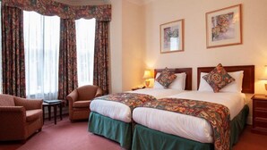 A hotel room with a large bed, two side tables, a chair, and a window with curtains. - Ashley Hotel (Cambridge)