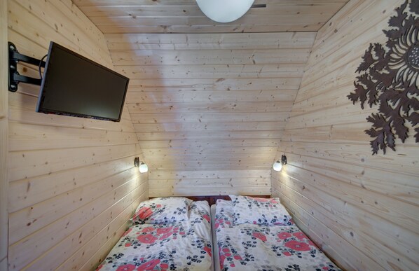 A wooden cabin room with two beds, a mounted TV, and wall-mounted lights.