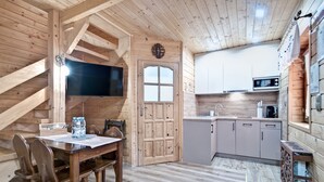 A wooden interior with a dining area, a kitchen, and a TV mounted on the wall. - Domki z Widokiem (Zakopane)