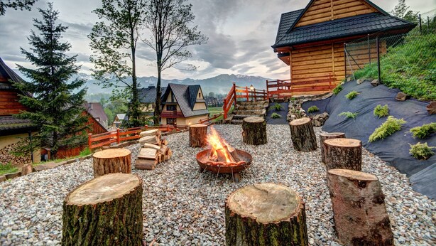 A rustic cabin with a fire pit surrounded by wooden stumps and a gravel path. - Domki z Widokiem (Zakopane)