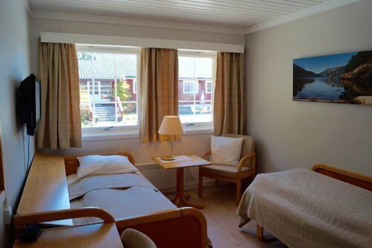 Hotellihuone, jossa on kaksi sänkyä, tuoli, pöytä ja taulu seinällä.