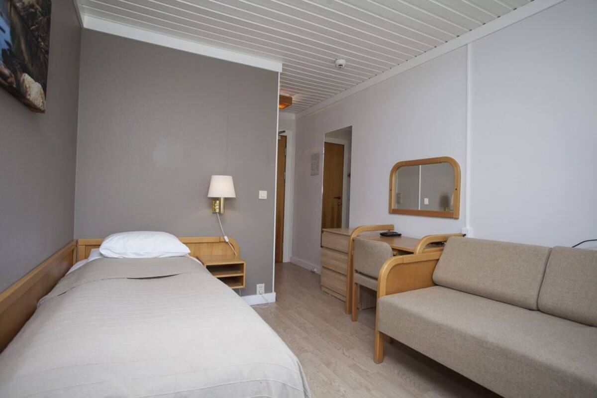Hotellihuone, jossa on sänky, työpöytä, tuoli, sohva, lamppu ja peili.