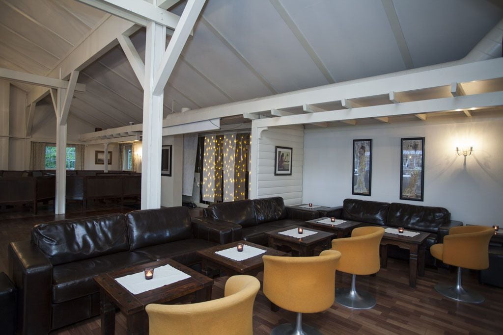 A spacious lounge area with leather sofas and yellow chairs, wooden tables, and framed pictures on the walls.