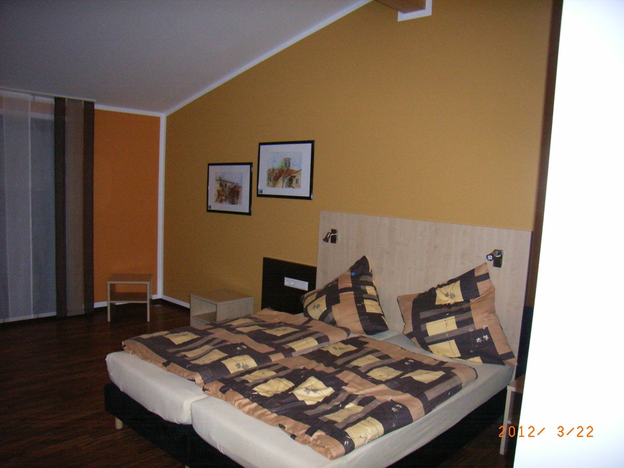 A bedroom with a bed, a nightstand, and two framed pictures on the wall.