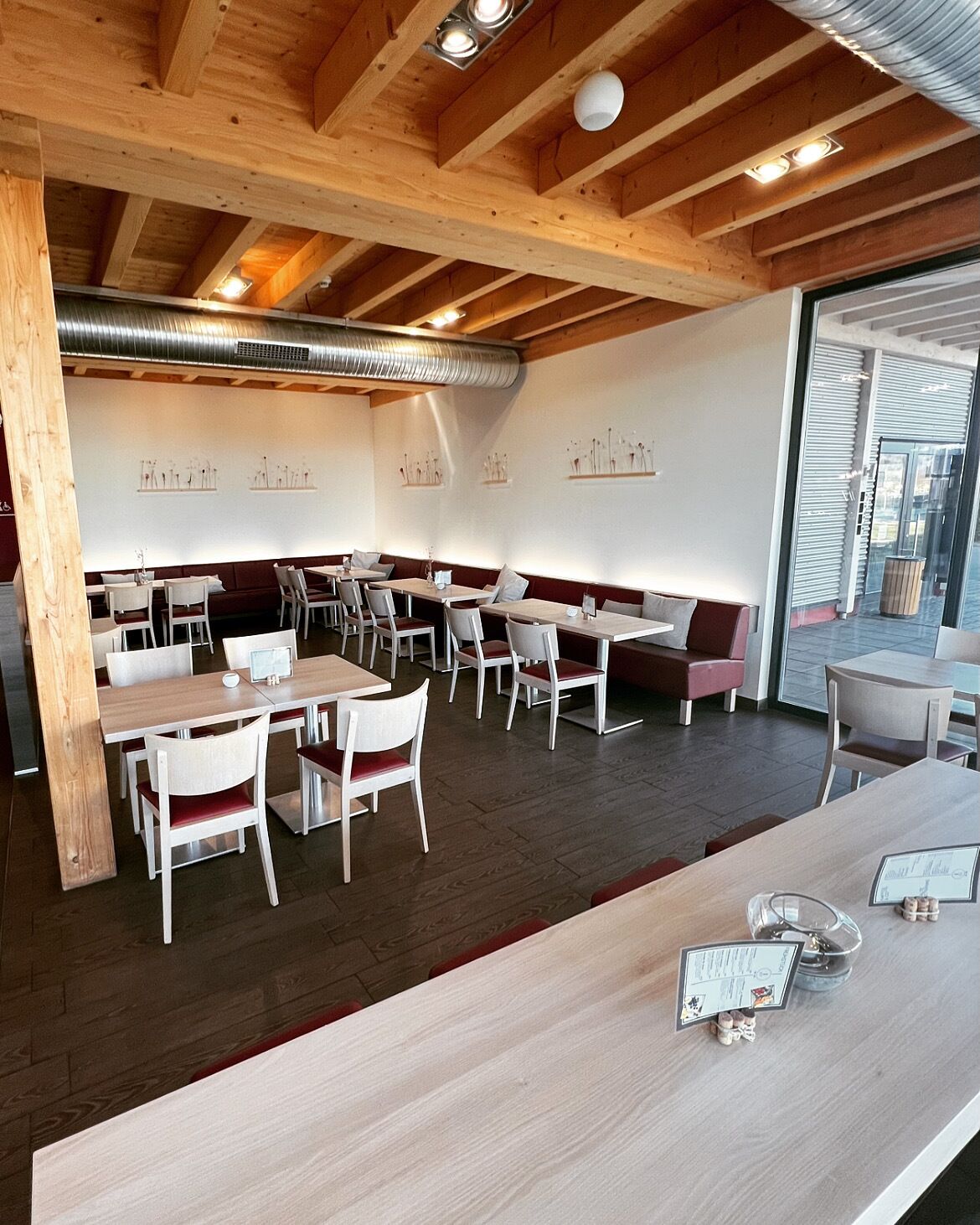 Un restaurant avec des poutres en bois, des chaises blanches et des tables. On y trouve des appliques murales et une grande fenêtre.