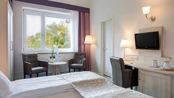 Habitación de hotel con cama, dos sillas, una mesita, televisor y ventana con cortinas.