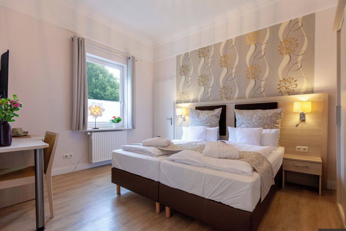 A bedroom with a large bed, bedside lamps, a desk, and a window with curtains.