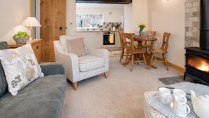 A cozy living room with a sofa, a patterned armchair, a dining table with chairs, and a fireplace.
