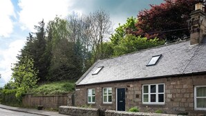 A stone cottage with a sloped roof, two windows with shutters, and a door.