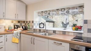 A modern kitchen with white cabinets, a wooden countertop, a built-in oven, and a window with decorative tiles.