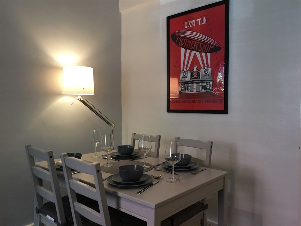 A dining area with a table set for four, a lamp, and a framed poster on the wall.