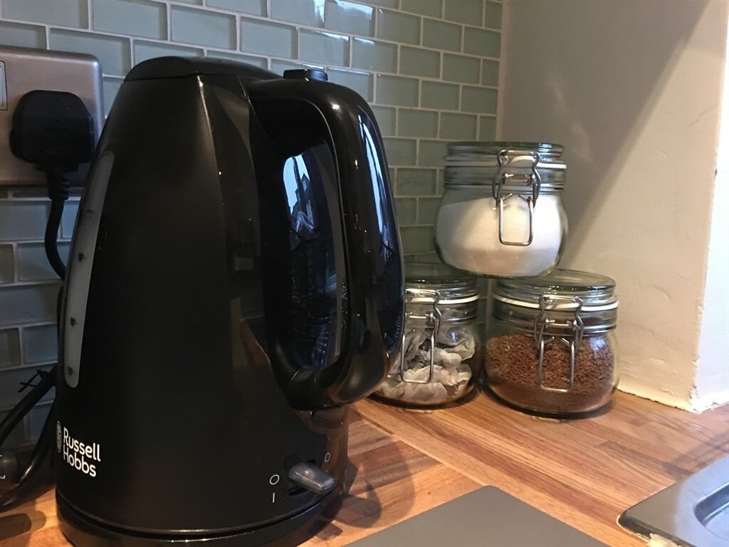 A kitchen with a black Russell Hobbs coffee maker, glass jars with sugar and coffee, and a tiled backsplash.