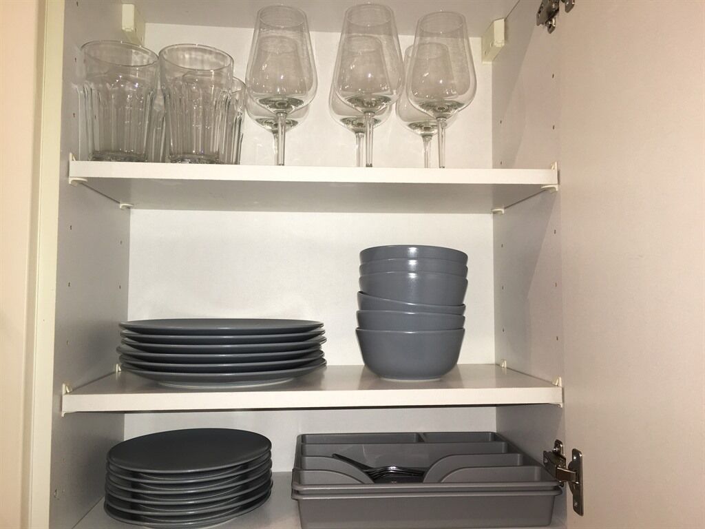 A storage cabinet with shelves holding wine glasses, plates, bowls, and a container.