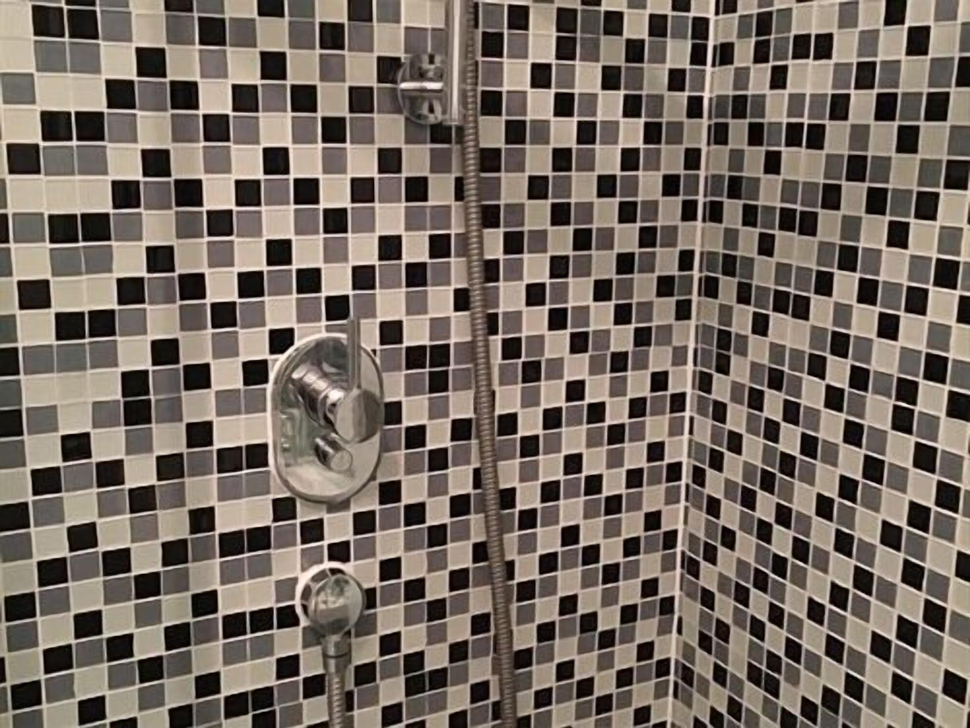 Une salle de bain avec un mur recouvert de carreaux à motifs et un panneau de commande pour la douche.